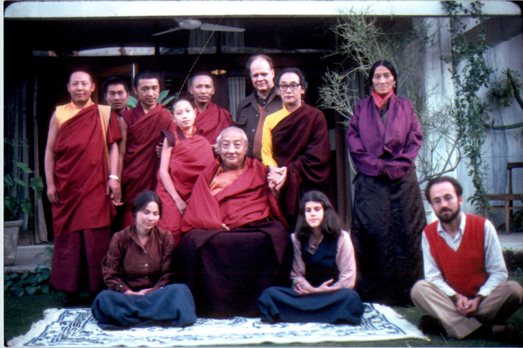 Dilgo Khyentse Rinpoche sitting on a chair in the middle and a group of people standing and sitting around him