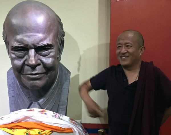 Dzongsar Khyentse Rinpoche standing next to a bust of Gene Smith